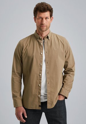 Chemise beige à manches longues, en coton, avec un col classique et des boutons blancs, superposée sur un t-shirt blanc.