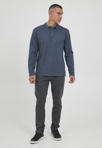 Marineblå langermet polo med krage, med knappelukking og logo på brystet. Kombinert med grå slim-fit bukser og svarte joggesko.