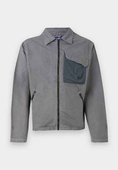 Veste grise avec un col, fermeture éclair devant et deux poches latérales. Présente une grande poche à patch texturée sur la poitrine gauche. Matériau en coton.