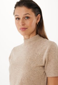 Svetlehnědý top s krátkým rukávem a vysokým límcem, vyrobený z měkké pleteniny s jemnou strukturou a vyváženým střihem.