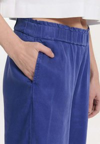 Blauwe broek van een gestructureerde stof, met een elastische tailleband en een zijzak. Het ontwerp is relaxed-fit voor comfort.