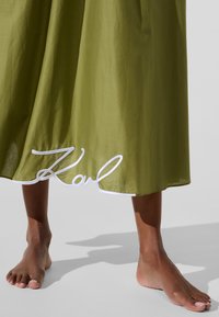 Õliveroheline seelik voolava disainiga; alläärsel valge tikandiga "Karl" detail. Pehme tekstuur, pahkluu pikkusega.