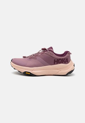 Buty do biegania w terenie Hoka w odcieniach różu i fioletu. Charakteryzują się teksturowanym materiałem, sznurowaniem i podeszwą Vibram zapewniającą przyczepność.