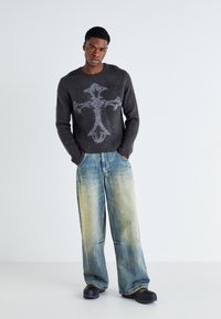 Dark gray fuzzy sweater with a cross design, paired with light blue wide-leg jeans featuring a gradient from blue to beige at the hem.