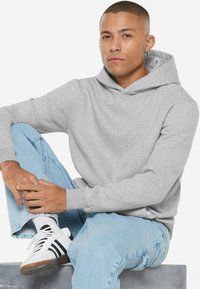 Gray hoodie with a kangaroo pocket, ribbed cuffs, and a drawstring hood. Paired with light blue jeans and white sneakers with black stripes.