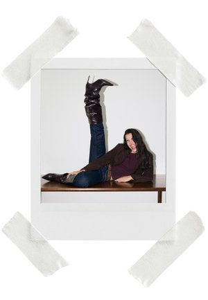 Glänzende burgunderfarbene Stiefel bis zum Knie mit einem lässigen Design, getragen mit blauen Jeans und einer braunen Jacke, vor einem schlichten Hintergrund.