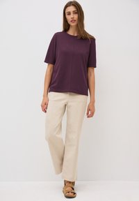 Korte mouwen, ronde hals t-shirt in donkerpaars, gecombineerd met beige wijde broek en bruine sandalen. Soepele textuur en ontspannen pasvorm.