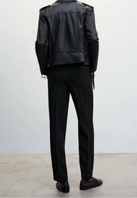 Sort lædermotorcykeljakke med kviltet tekstur, parret med sorte skræddersyede bukser og sorte sko, set fra ryggen.