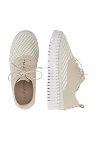 Zapatos beige de cordones con textura trenzada en la parte superior, suela blanca en contraste con relieve, y puntera redondeada. Diseño minimalista con líneas limpias.