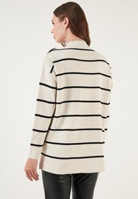 Maglione beige a righe con linee orizzontali nere, caratterizzato da un collo alto e una vestibilità rilassata. Il tessuto sembra morbido con una trama minima.