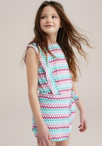 Prenda de tela ligera con un patrón de zigzag multicolor. Presenta mangas tipo capa y un cinturón en la cintura. Los colores incluyen rosa, azul y blanco.