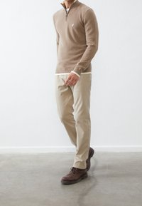 Beige zip-up tröja med smal passform, kombinerad med ljusbeige byxor. Bruna snörstövlar fulländar outfiten. Mjuk textur, avslappnad design.