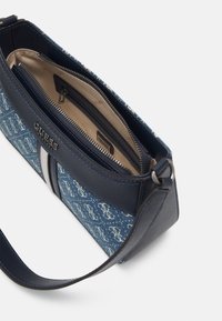 Blaue und weiße Guess-Handtasche mit Monogramm-Muster, marineblauen Lederakzenten, sichtbarem Reißverschlussfach und einem einzelnen Schulterriemen.