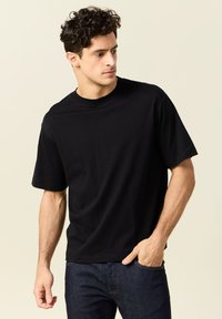 T-shirt nera a maniche corte realizzata in morbido cotone. Design semplice con scollo rotondo e vestibilità rilassata, abbinata a jeans scuri.