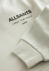 Manica di felpa bianca con il testo nero "ALLSAINTS", caratteri giapponesi e "LONDON" stampato sul tessuto.