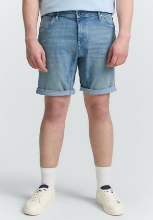 Shorts en denim bleu clair avec des retroussés, dotés de poches avant et d'une fermeture éclair. Portés avec des baskets blanches et des chaussettes de longueur mi-mollet.