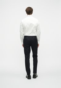 Camisa branca de botões e calças de fato azul-marinho, combinadas com sapatos pretos. Tecido suave com um corte ajustado e perna reta. Detalhes mínimos.