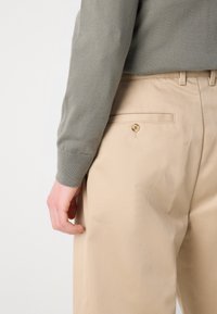 Beiga byxor med en slät textur, utrustade med en bakficka och knäppning med knapp. Outfiten kompletteras av en grön stickad tröja.