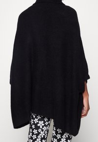 Czarny dziany poncho z golfem, luźny krój i miękka textura. W połączeniu z wzorzystymi, białymi leginsami w kwiaty.