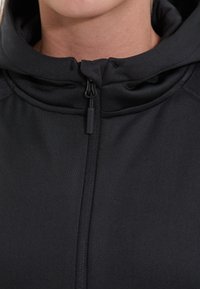 Zwarte zip-up hoodie met hoge kraag en zachte textuur, voorzien van een centrale rits en verstelbare trekkoorden bij de capuchon.