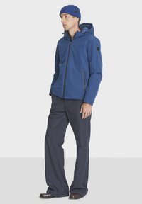 Blue waterproof jacket with a hood, zippered front pocket, and elastic cuffs, paired with dark blue pants and a blue knitted beanie.