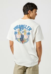 Camiseta blanca de algodón con un gráfico colorido de sirena y el texto "WRANGLER" en la parte trasera, con motivos de palmeras y olas.