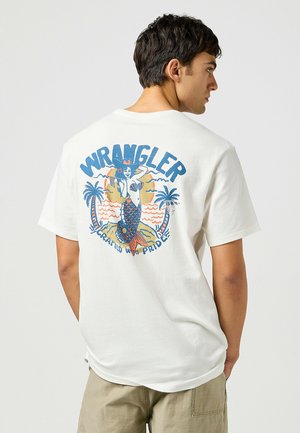Camiseta blanca de algodón con un gráfico colorido de sirena y el texto "WRANGLER" en la parte trasera, con motivos de palmeras y olas.