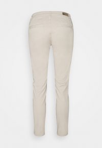 Pantalones ajustados beige con una textura suave. Presentan dos bolsillos traseros y una sutil etiqueta de la marca cerca de la cintura. Diseño clásico.