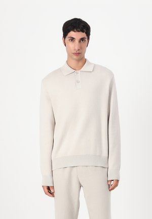 Lys beige skjortepiké med lange ermer, ribbestrikkede mansjetter og teksturert overflate. Brukt sammen med matchende lyse bukser.