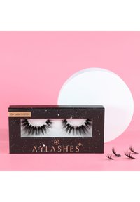 Black false eyelashes in a clear display case with a black and gold label. Includes additional smaller lashes beside the case on a pink background.