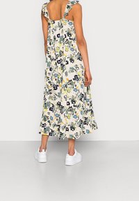 Robe midi florale avec des bretelles froncées, arborant un fond crème et des fleurs bleues, vertes et jaunes. Assortie à des baskets blanches.