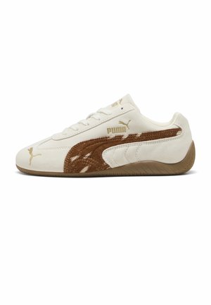 Zapatilla blanca Puma con franja de ante marrón y suela de goma, con cordones, mostrando el perfil derecho sobre fondo blanco.