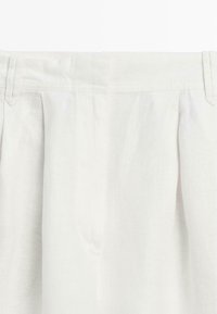 Pantaloni di lino bianco con pieghe e passanti per cintura, mostrati dalla vita in giù.