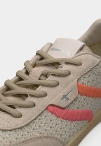 Baskets beiges avec une tige en mesh texturé, des lacets gris, et des accents orange vif et rose. Présentent un logo argenté sur le côté.