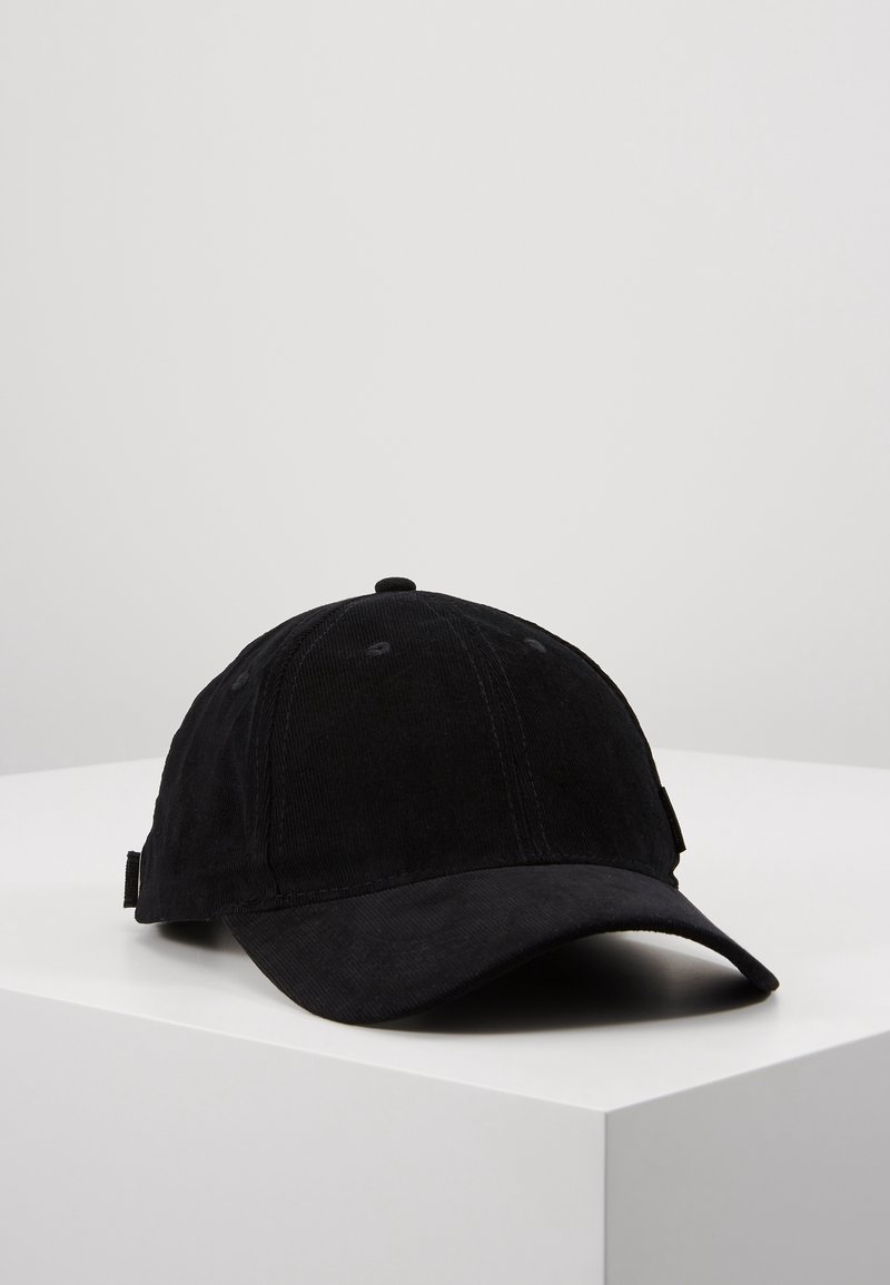 Casquette de baseball noire à visière incurvée posée sur une surface blanche devant un fond gris clair uni.