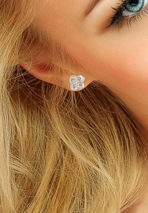 Boucles d'oreilles en argent au design entrelacé ornées de pierres précieuses transparentes, présentées sur l'oreille d'un modèle avec de longs cheveux blonds.