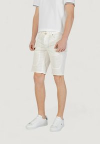 Pantalones cortos blancos con una textura suave, bolsillos frontales y costuras visibles. Llevados con una camisa blanca y zapatillas blancas con detalles en azul marino.