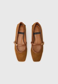 Ballerines en suede marron avec un bout carré, une sangle ajustable et des accents en cuir. La doublure intérieure est en matériau marron lisse.