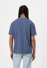 T-shirt de algodão azul escuro, de manga curta e decote redondo. Apresenta um corte reto e detalhes de costura subtil. Vista traseira lisa.