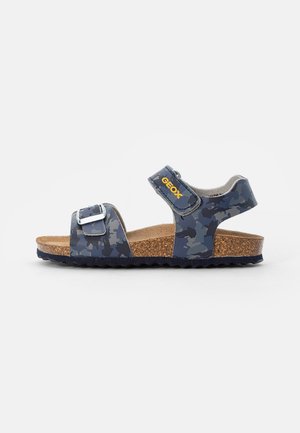 Barns blå camouflage sandal med justerbar spænde og velcro stropper samt korksål på hvid baggrund.