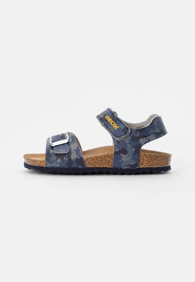 Sandale enfant camouflée bleue avec boucle réglable, brides en velcro et semelle en liège sur fond blanc.