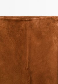 Brun konstmocka med en mjuk textur, som har en vertikal söm ner i mitten och en ren, enkel design.