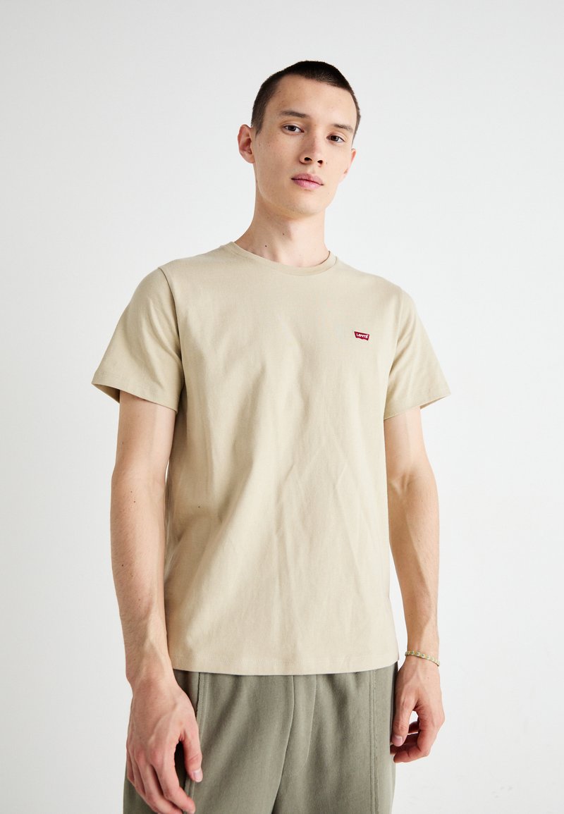 T-shirt in cotone beige con scollatura rotonda, maniche corte e un piccolo logo rosso di Levi's sul petto sinistro. Morbido al tatto, vestibilità casual.