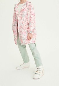Veste imperméable rose clair à fleurs avec fermeture éclair, poignets élastiques, deux poches avant, associée à un pantalon vert menthe et des baskets blanches avec des accents.