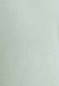 Tissu tricoté gris clair avec un motif subtil en forme de losange et une texture douce, éclairé uniformément pour montrer le tissage détaillé.