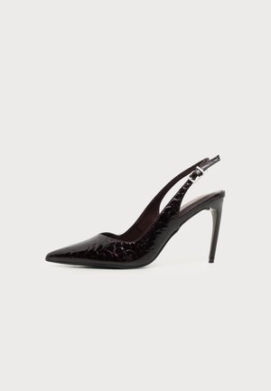 Zapato de tacón alto tipo slingback de charol negro con puntera puntiaguda y correa ajustable con hebilla sobre fondo claro liso.