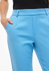 Lyseblå skreddersydde bukser laget av glatt stoff, med flatt frontstykke, sidelommer og beltehemper, med en tettsittende silhuett.