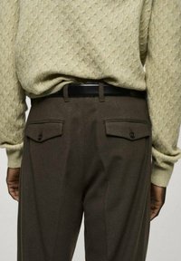 Pull en kaki avec un motif texturé associé à un pantalon marron foncé avec des poches arrières et une ceinture noire.