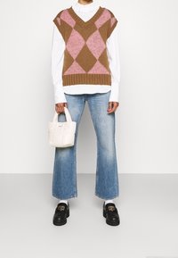 Chaleco de punto en patrón argyle marrón y rosa sobre una camisa blanca de manga larga, combinado con jeans de tiro alto de color azul claro y zapatos de plataforma negros. Pequeño bolso blanco.