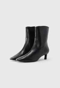 Botas pretas de salto curto feitas em couro liso, com bico pontiagudo, salto bloco baixo, fecho lateral de correr e design elegante.